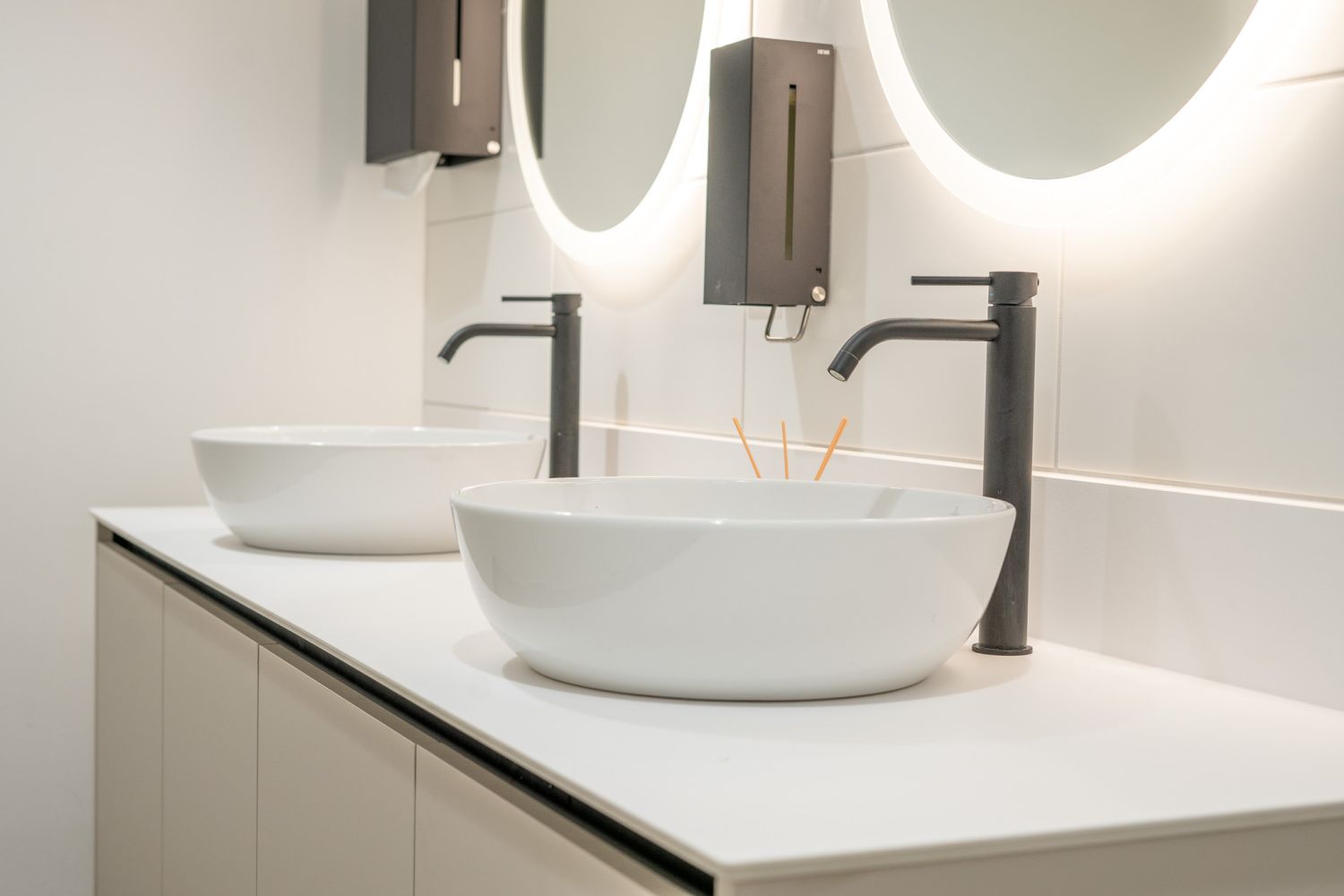 Objekteinrichtung-Waschtisch-mit-Aufsatzwaschbecken-und-Unterschrank-runde-beleuchtete-Spiegel-und-schwarze-Armaturen